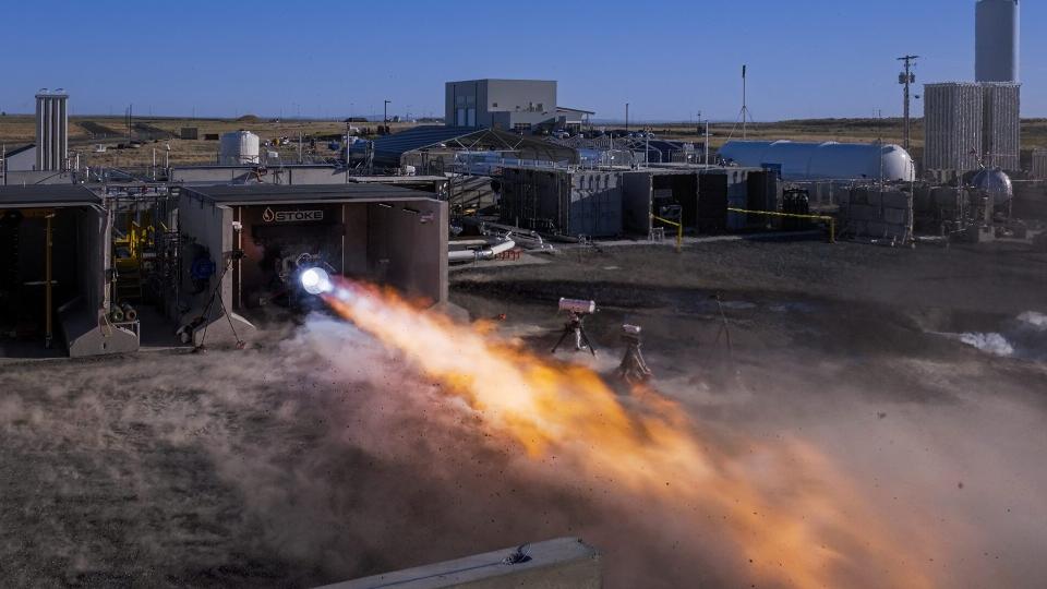 a rocket engine sits horizontally on a test stand outside, belching hot fire