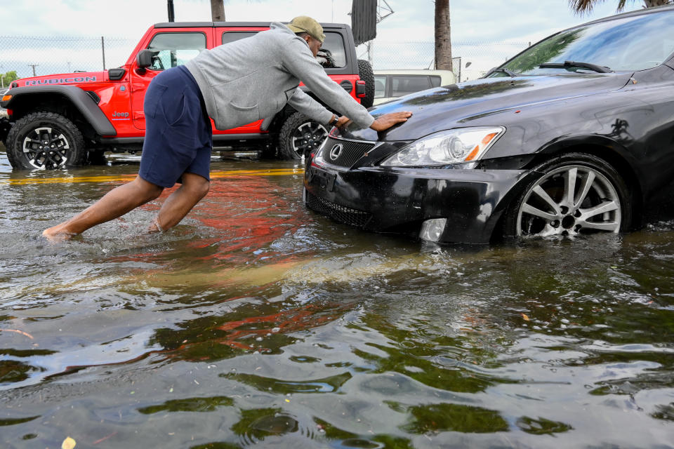 A man pushes a car on a flooded street. 