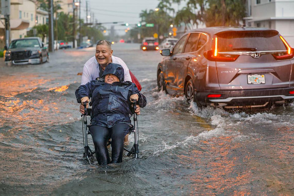 A man pushing his wife in a wheelchair through floodwaters.