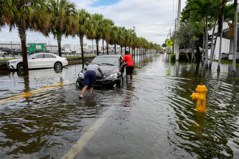 Two people push a car along a flooded street on Thursday in South Florida. 