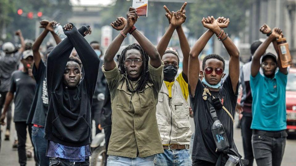 Protesters with arms aloft shout slogans at riot police during a protest to oppose a proposed Finance Bill 2024, in Nairobi, Kenya, 18 June 2024