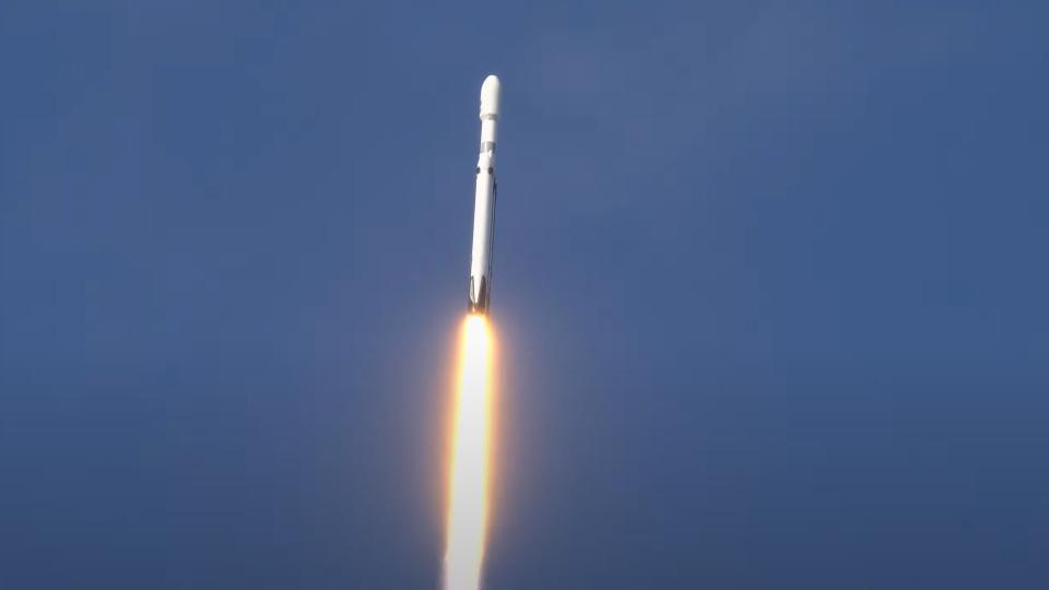 a large white rocket launches through a clear blue sky