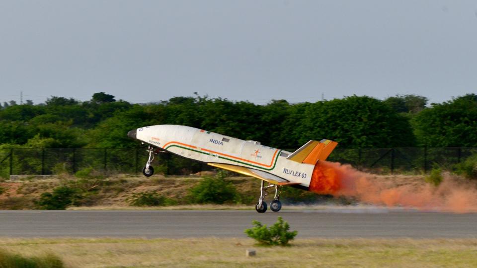 a white aircraft with no windows or cockpit canopy lands on a runway surrounded by tropical vegetation