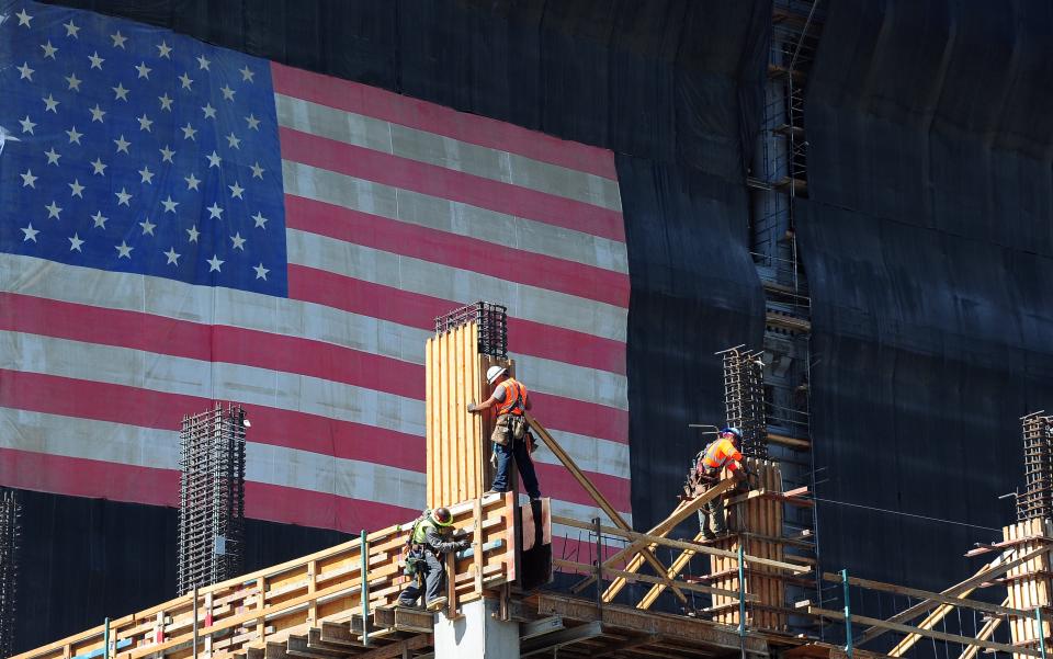 Construction workers work the construction of a new building partly covered with a large US flag on September 25, 2013 in Los Angeles, California, where the state's Governor Jerry Brown signed legislation  that will raise the California minimum wage from $8 to $10 per hour by 2016. AFP PHOTO/Frederic J. BROWN        (Photo credit should read FREDERIC J. BROWN/AFP via Getty Images)