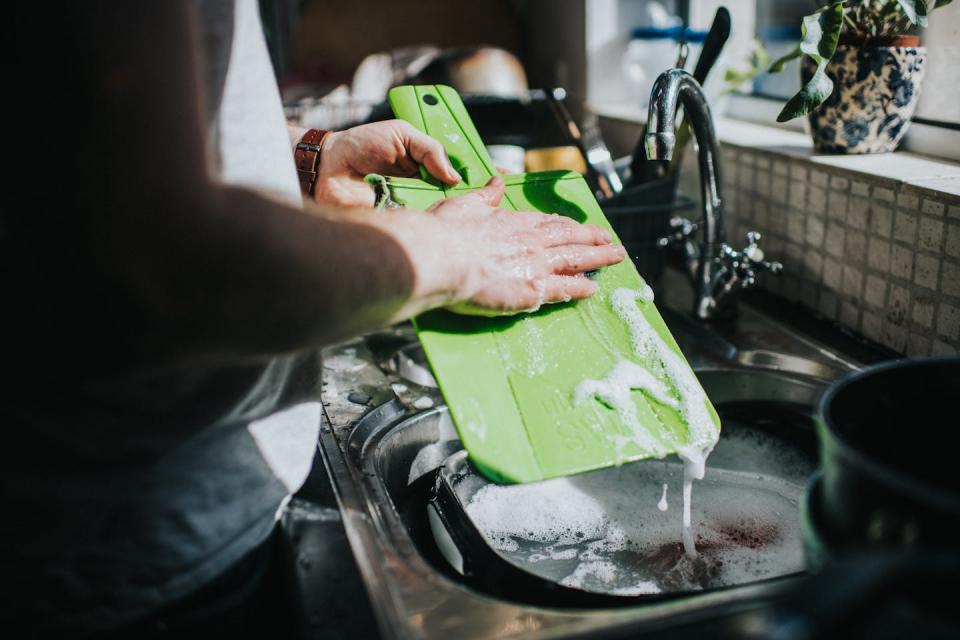 Person washing a cutting board in the kitchen sink