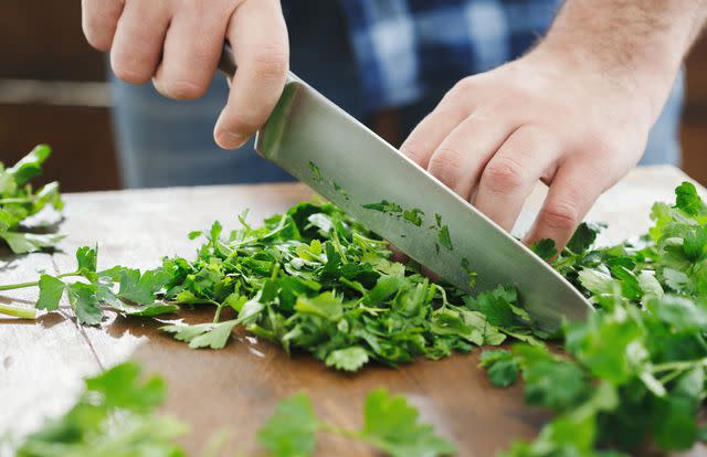 <p>KucherAV / Getty Images</p> Person chopping cilantro on wooden table close up