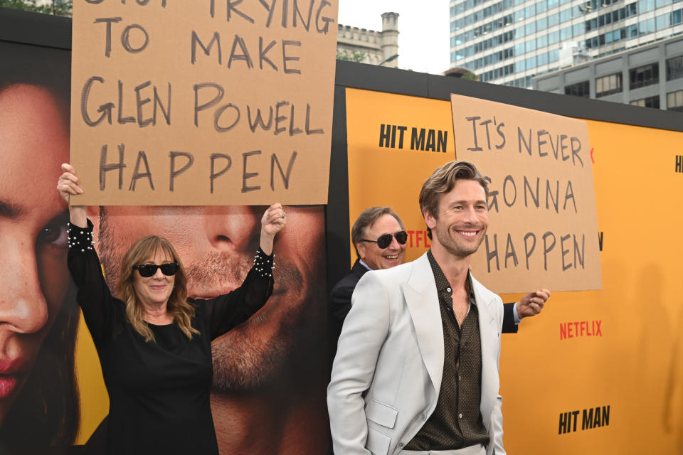 Glen Powell in front of his parents holding up signs.