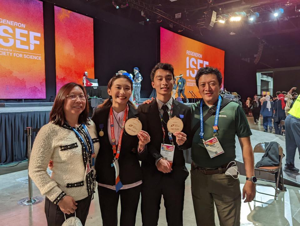 four people standing in front of a stage wearing lanyards two young people in the middle holding up round brown medals