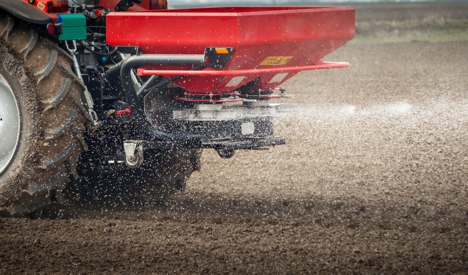 The back of a tractor throwing out small fertilizer pellets, about the size of peas.