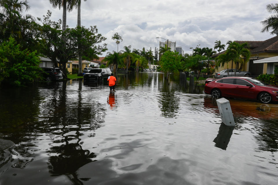 A man in a bright orange shirt walks along a flooded street of South Florida.