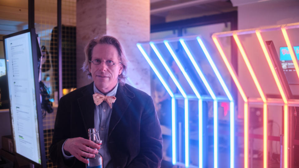 a man in a suit and holding a glass bottle of mineral water stands in front of a series of lamps