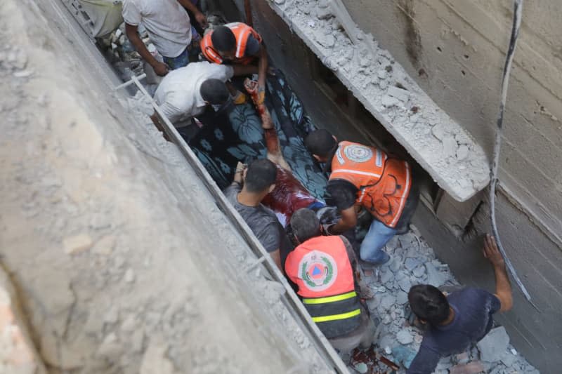 Rescuers and civilians remove the body of a man from under the rubble following an Israeli strike on the Nuseirat refugee camp. Omar Ashtawy/APA Images via ZUMA Press Wire/dpa