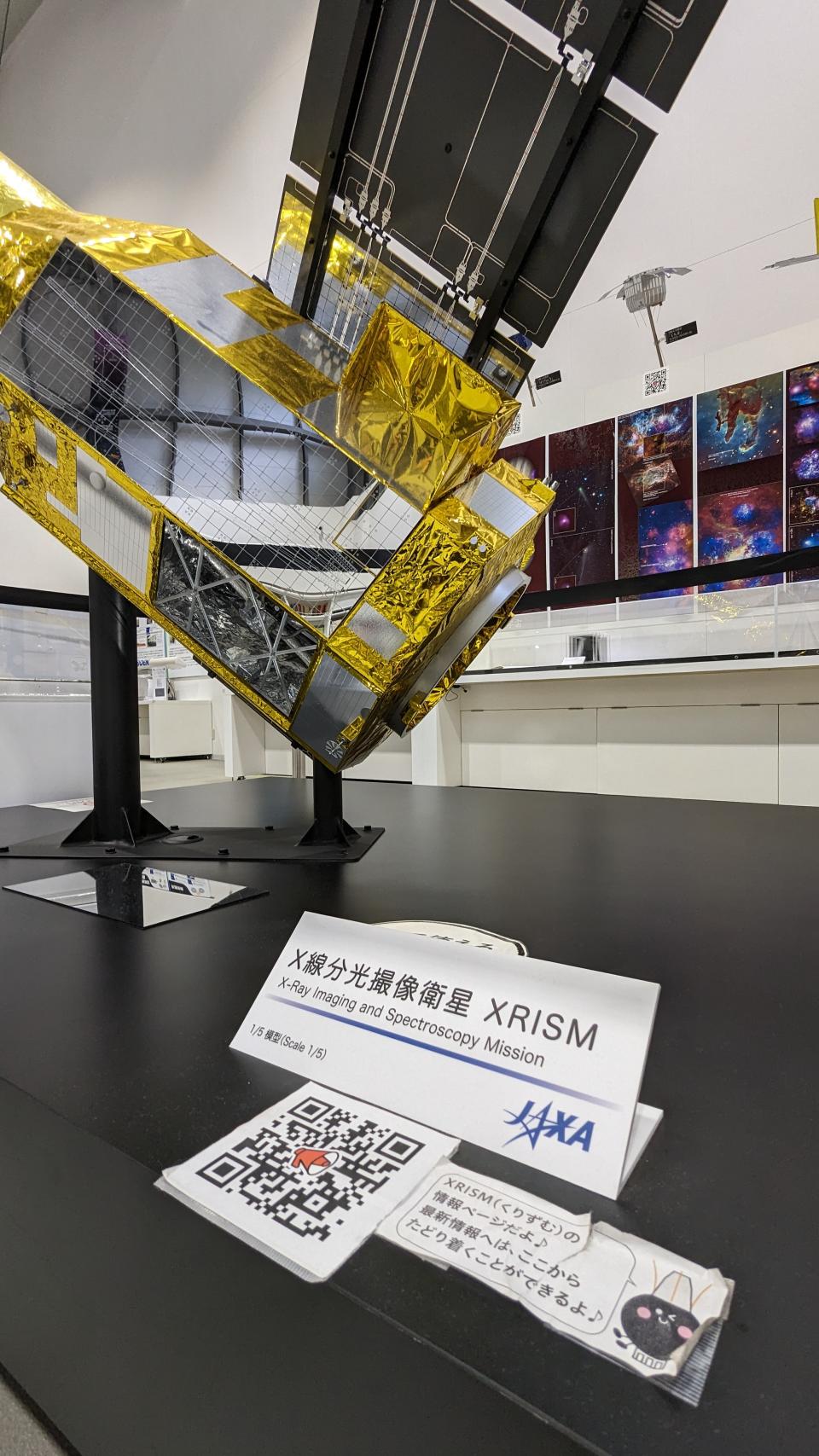 A display piece in a museum-like environment showing the XRISM spacecraft as a model.