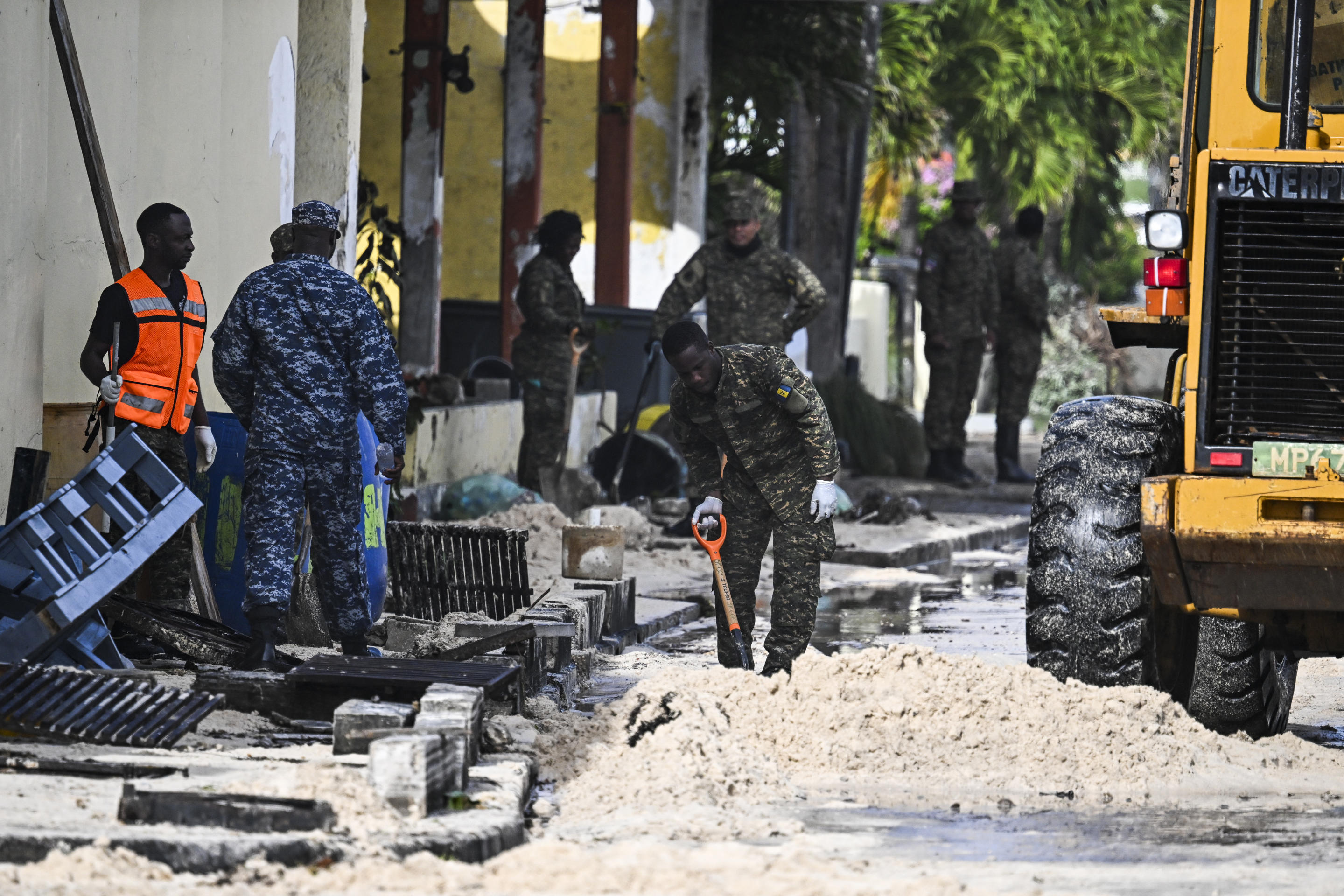 Several members of the Barbados armed forces use shovels to clear a street of sand after it was flooded by seawater.