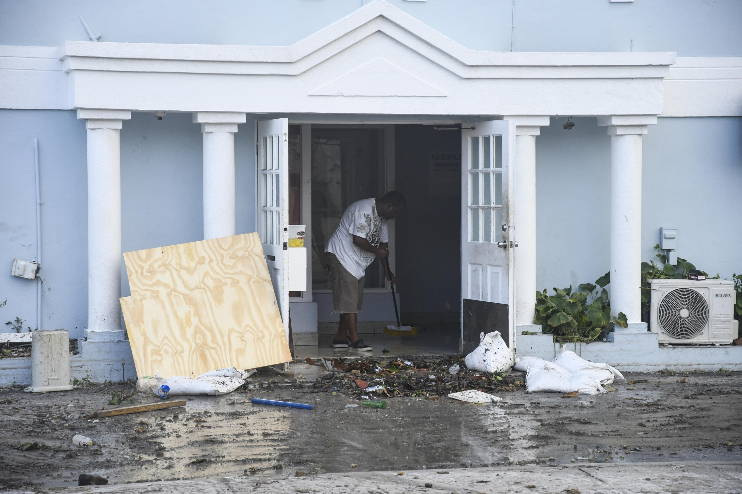 A man uses a broom to clear water from the front of a damaged restaurant in Christ Church, Barbados. 