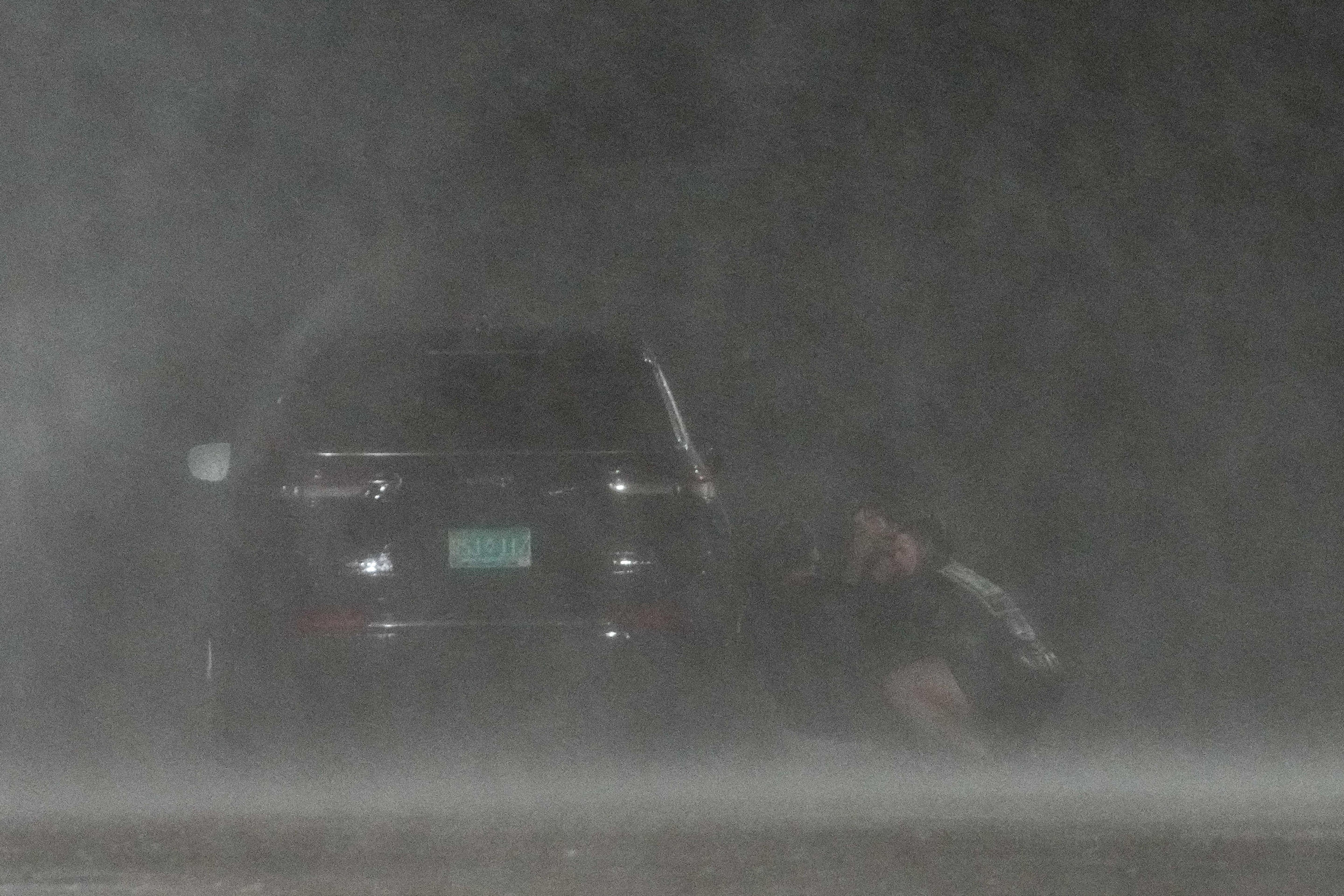 People hide behind a car to shield themselves from wind and rain as they film videos for social media in Bay City, Texas, on Monday. 