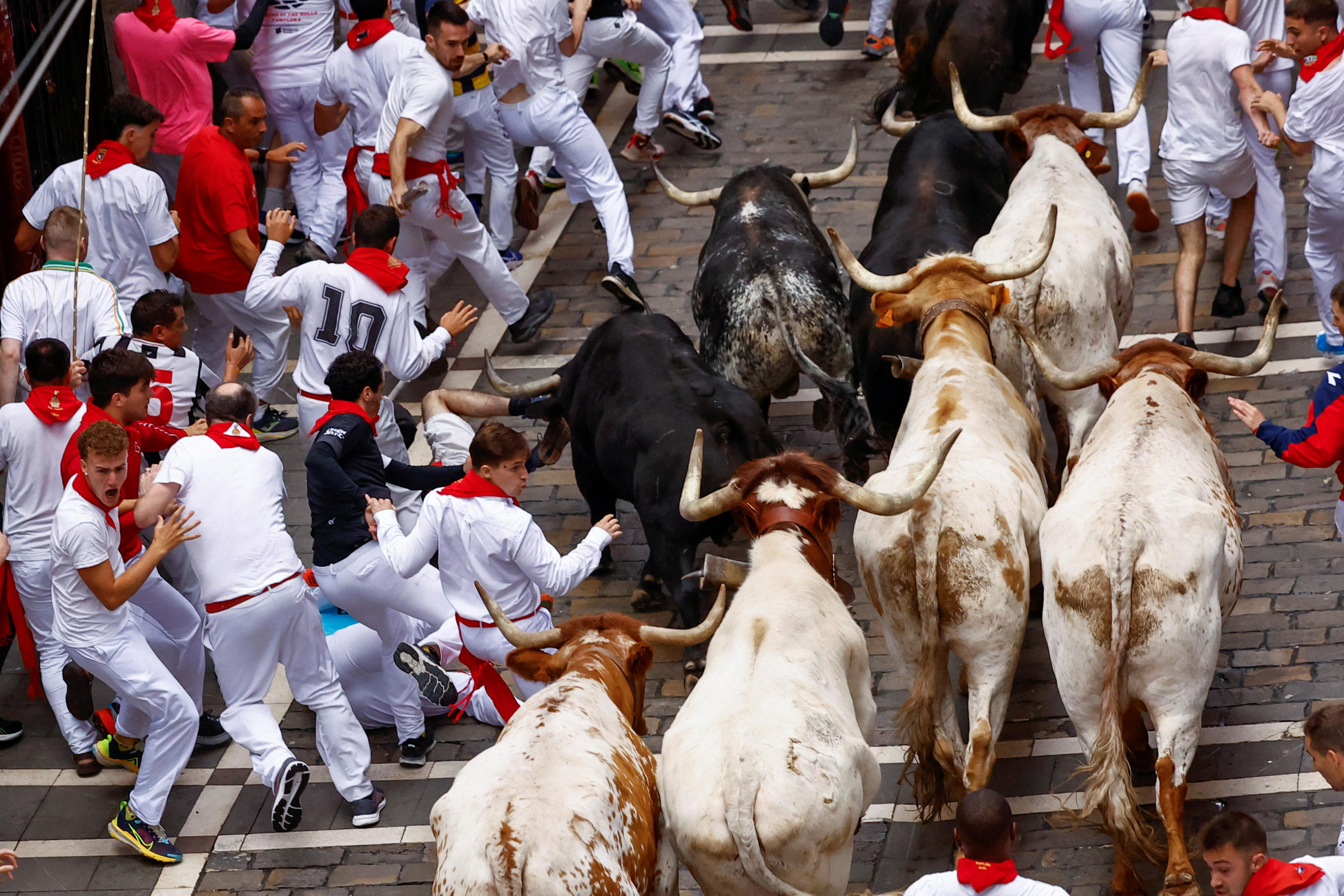 Festival participants run alongside but out of the way of bulls charging down a narrow alleyway.