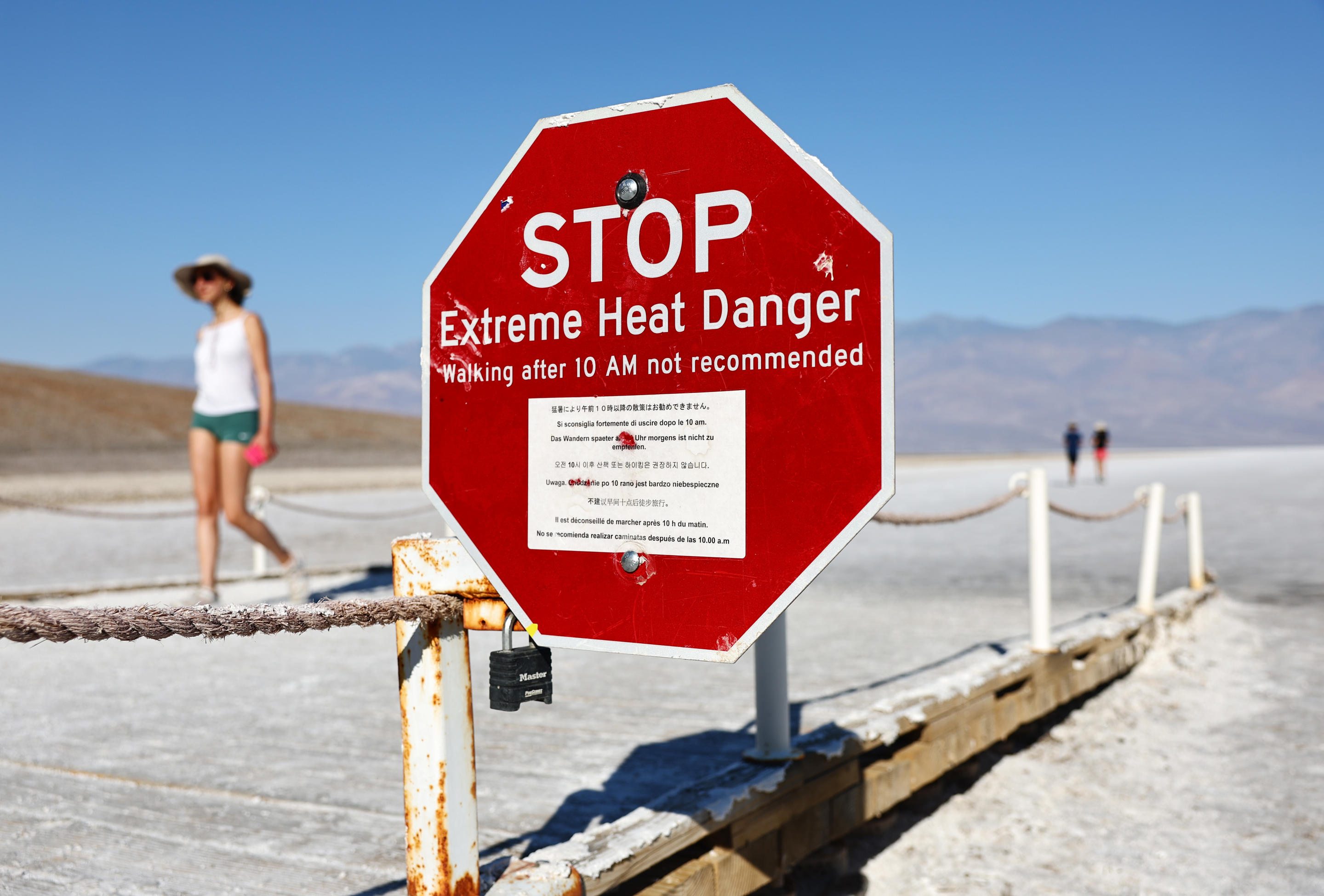 Visitors walk near a sign that reads: Stop — Extreme Heat Danger