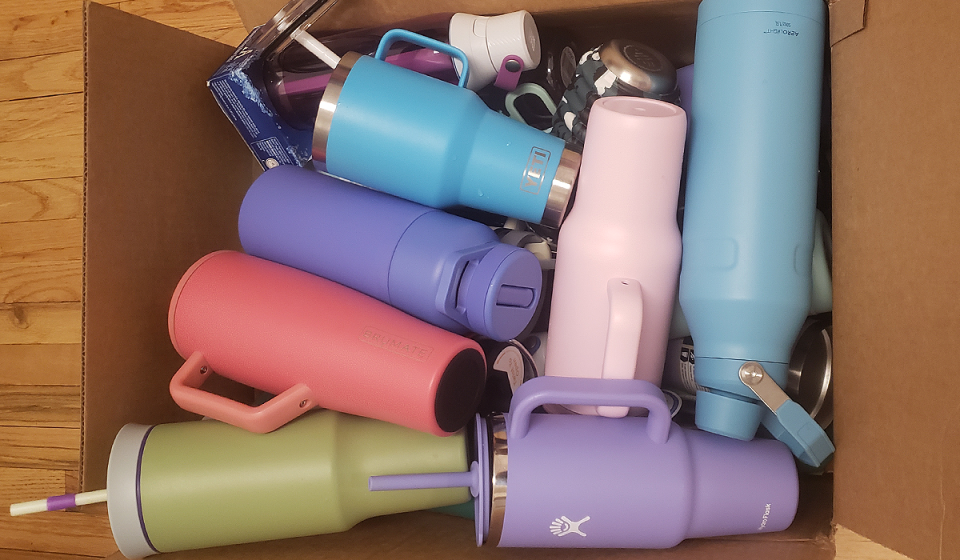 A bunch of water colorful bottles and tumblers shown in a cardboard box, to be tested for Yahoo's best water bottle guide