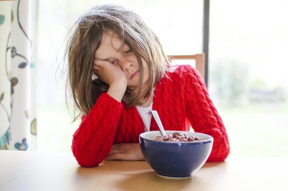 Sleepy young girl at the breakfast table, face in hand.