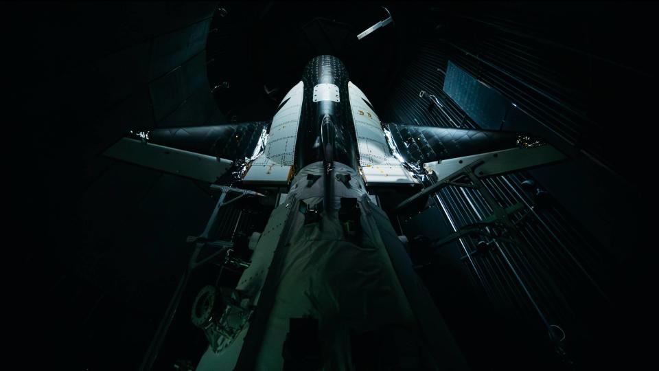 a black-and-white winged spacecraft stands upright inside a silo-like structure