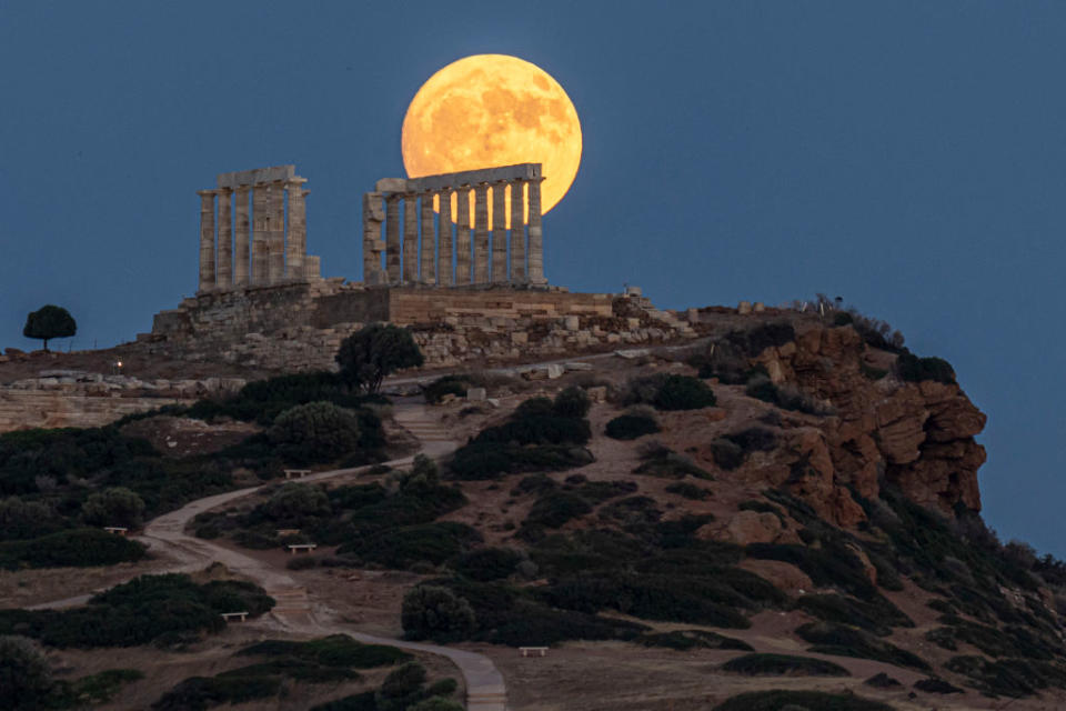 bright large full moon behind temple ruins of numerous columns standing tall.