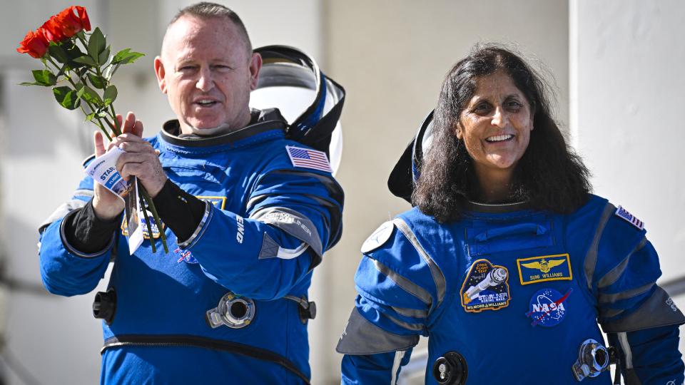 two astronauts in spacesuits. the man on the left holds roses