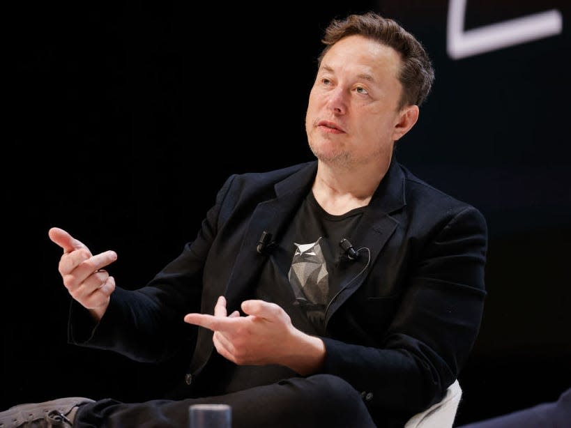 Elon Musk wearing a black sport jacket and T-shirt, speaking onstage at Cannes Lions.