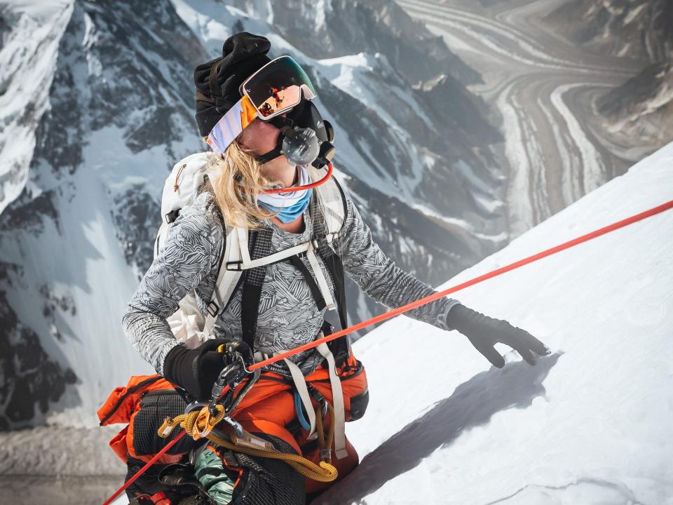 A woman in climbing gear kneels on the side of K2