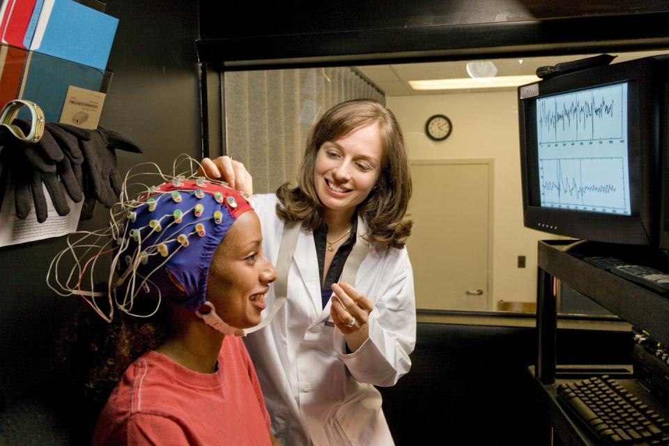 Young woman wearing a cap with electrodes connected to a computer.