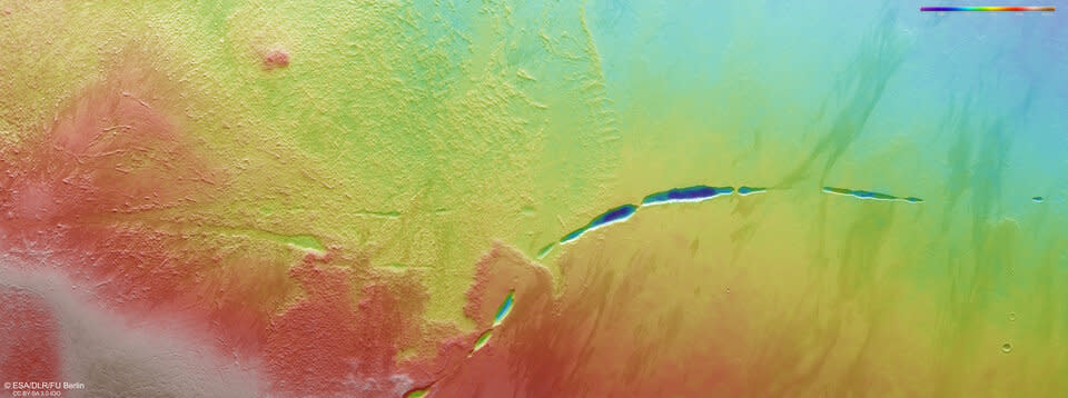 a rainbow landscape seen from space shows a swath split in two by a winding, segmented canyon.