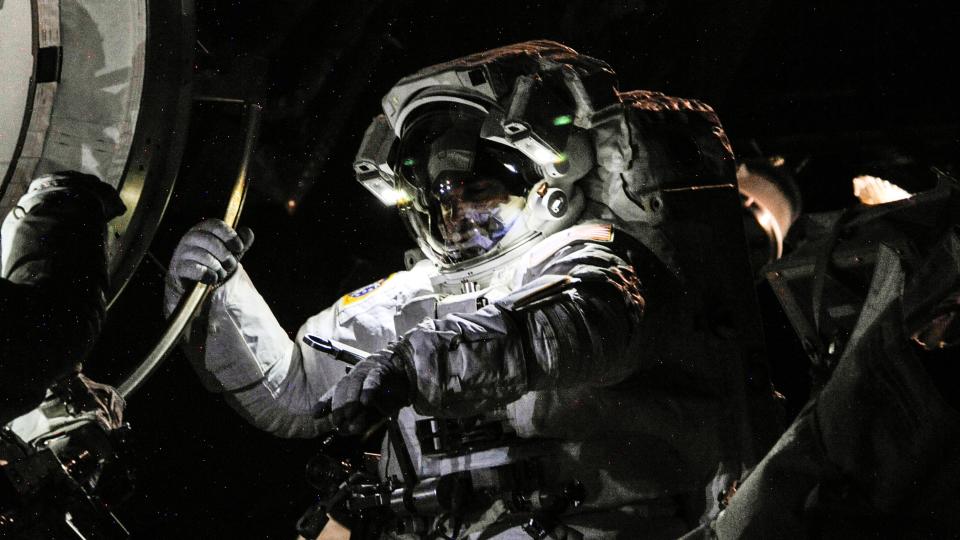  A ghostly lit picture of astronaut chris cassidy in a spacesuit in space. the astronaut holds on to the international space station hatch with his right hand. 