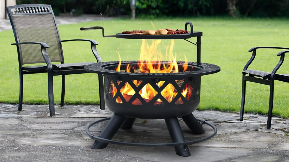 fire pit with grill grate on top next to two chairs outdoors