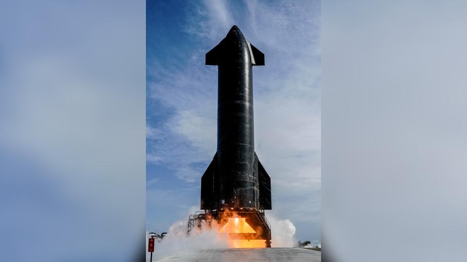  A sleek black rocket fires its engines while stationary on a launch pad. 