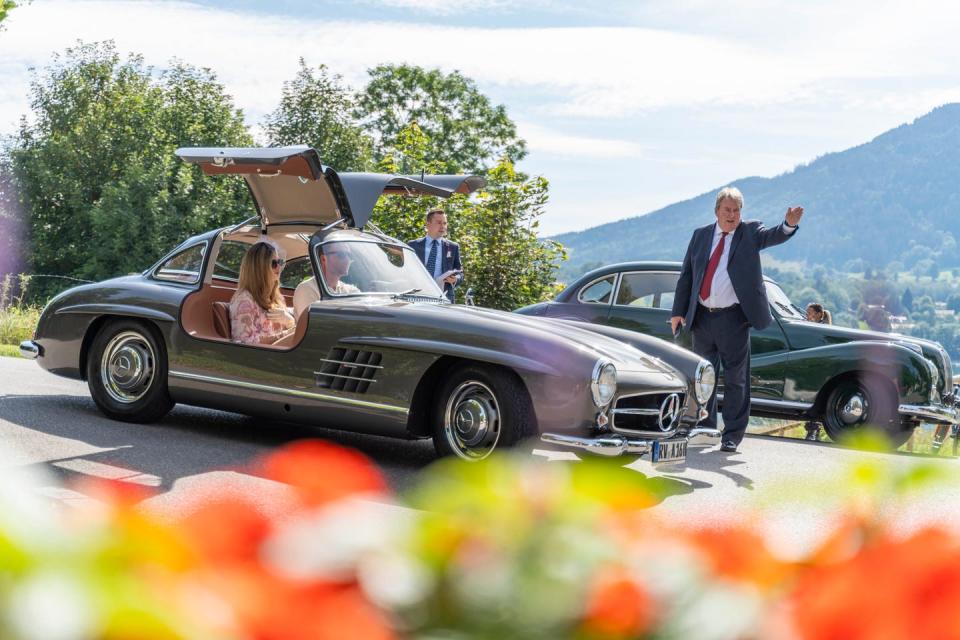 a man standing next to a mercedes 300 sl with a woman in it