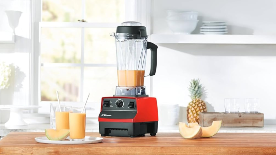 A red Vitamix blender on a kitchen counter next to two cups holding smoothies