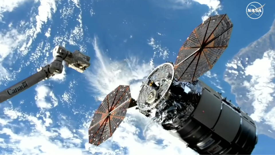 a cylindrical spacecraft approaches the international space station with earth in the background