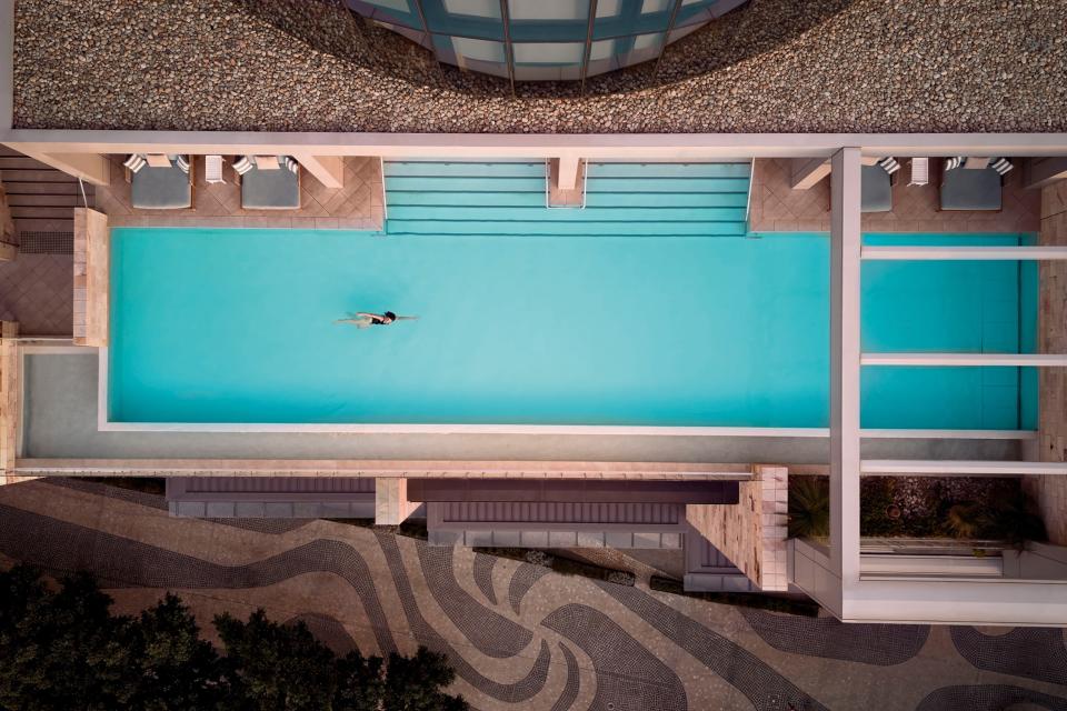 Birds eye view of a woman swimming in an empty turquoise swimming pool