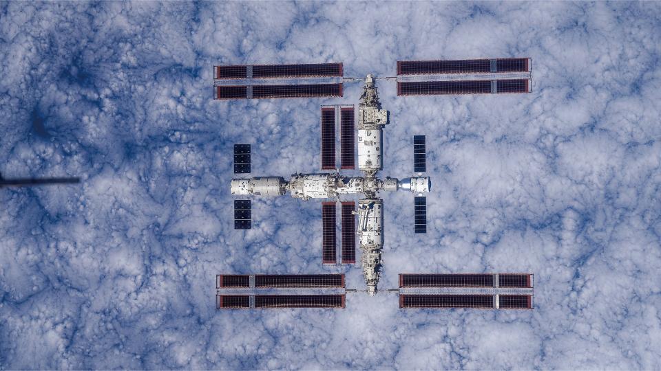 a large T-shaped space station is seen from above with Earth below it