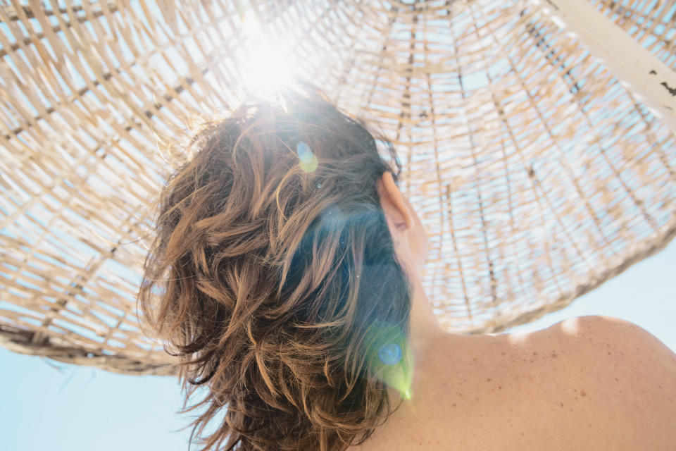 woman and her hair from the back under a white straw sunshade 