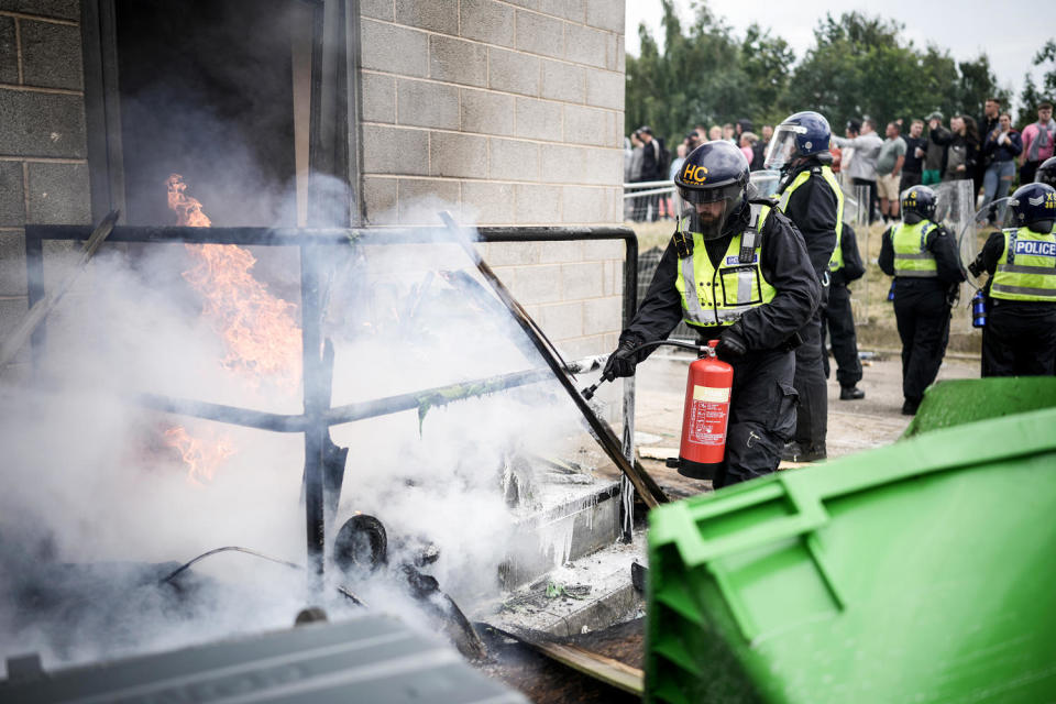 A Riot police officer uses a fire extinguisher on a fire in front of a doorway billowing smoke (Christopher Furlong / Getty Images)