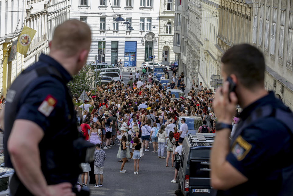 Two police officers have faces turned toward a few hundred people along a street.