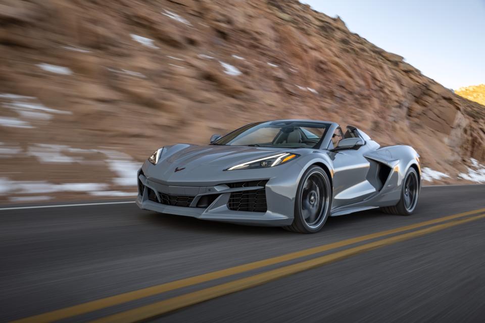 Front 3/4 view of a 2024 Corvette E-Ray 3LZ convertible in Sea Wolf Gray Tricoat driving on a mountain road. Pre-production model shown. Actual production model may vary. Model year 2024 Corvette E-Ray available 2023.