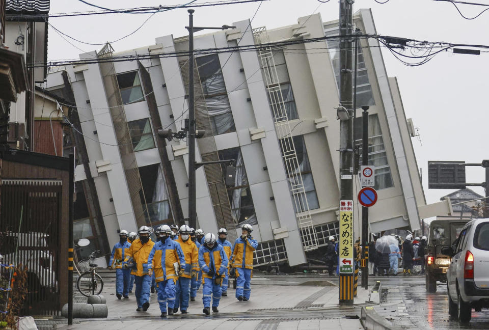 Firefighters walk near a fallen building following earthquakes in Wajima, Ishikawa prefecture, Japan Wednesday, Jan. 3, 2024.  (Kyodo News via AP)