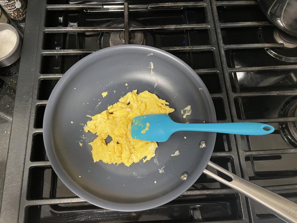 Guy Fieri's Flavortown Laser Titanium Frying Pan with scrambled eggs and a spatula on stovetop