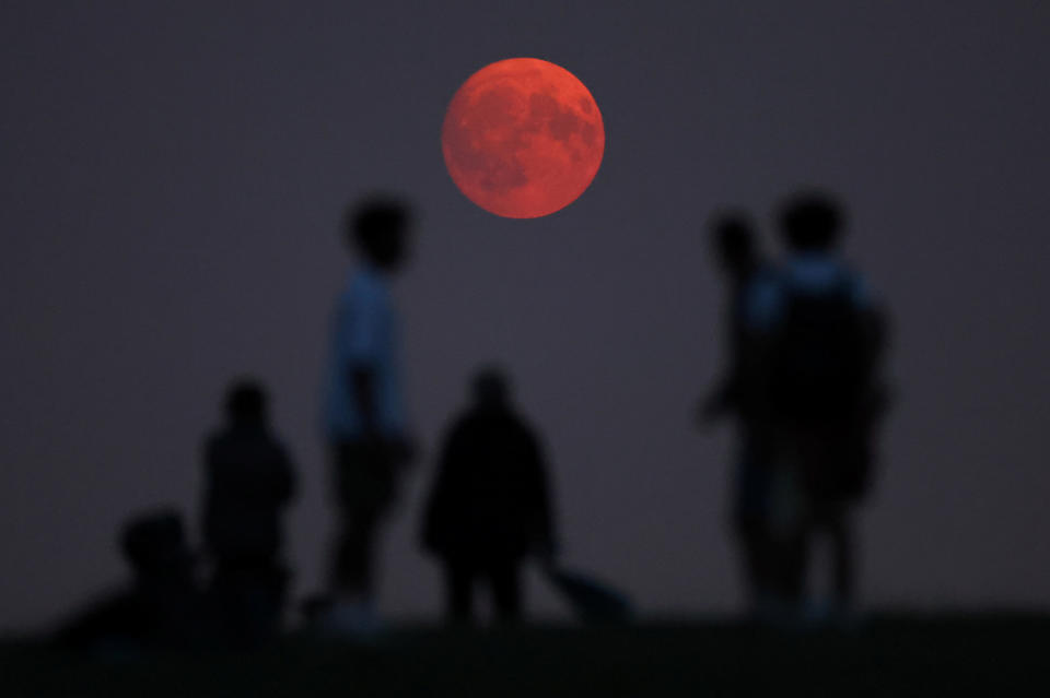 People view the moon as it rises, with a red glow attributable to smoke particles carried in the upper atmosphere from North American wildfires, a day ahead of the full super moon, at Parliament Hill in London, Britain, on Aug. 18, 2024. / Credit: Toby Melville/REUTERS