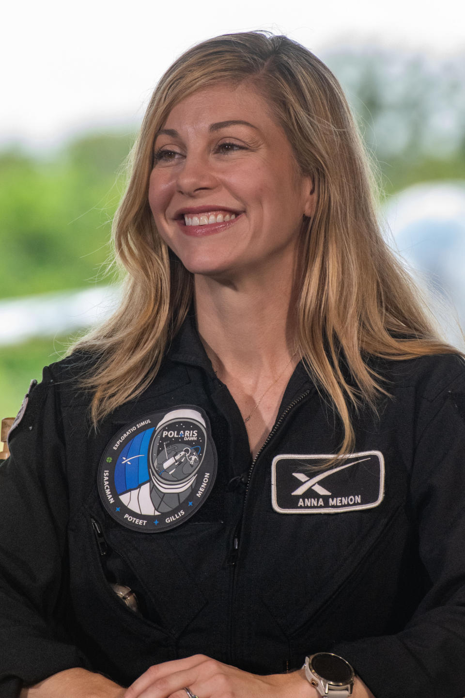 A blond woman in a dark jumpsuit is smiling.