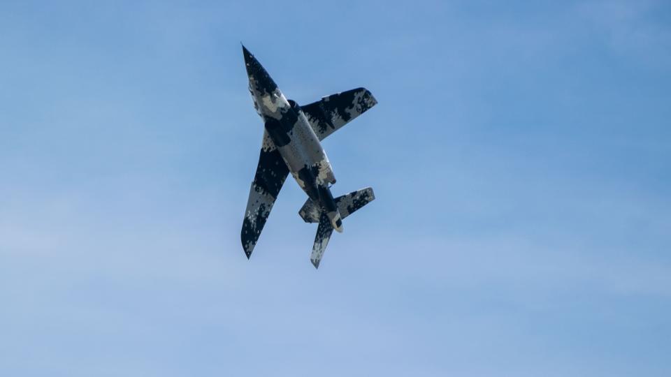 A blue and white camoflouge plane flies in the sky.