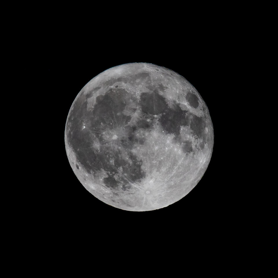 A fully illuminated moon against a black backdrop of night sky.