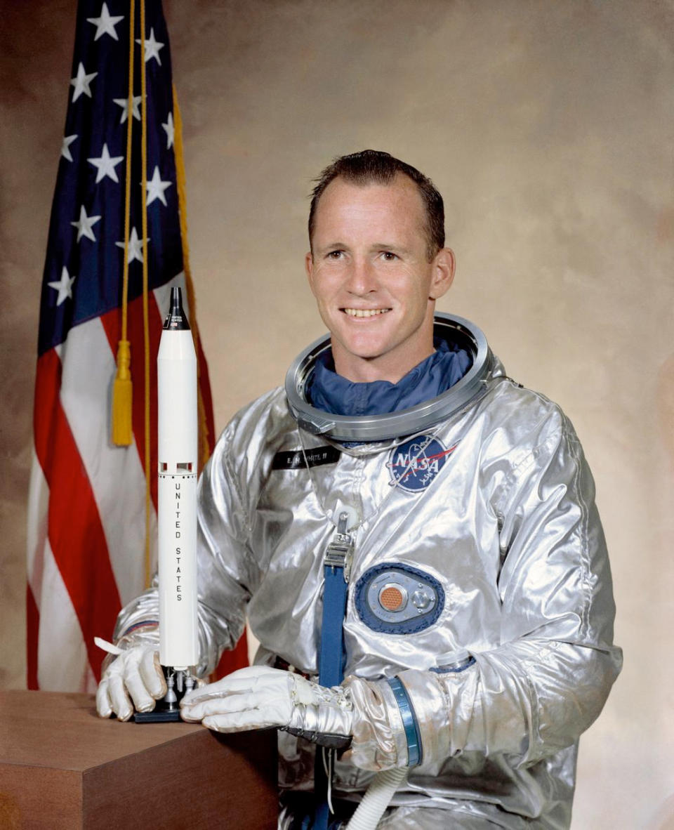 a man in a silver flight suit posing for a portrait beside a model rocket